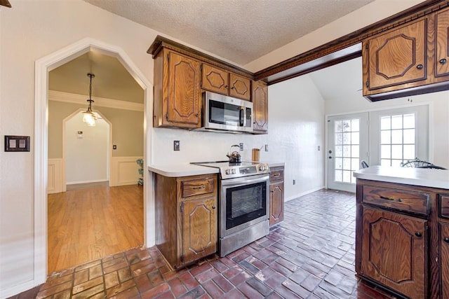 kitchen with brick floor, pendant lighting, stainless steel appliances, light countertops, and wainscoting