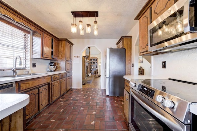 kitchen with arched walkways, hanging light fixtures, stainless steel appliances, light countertops, and a sink