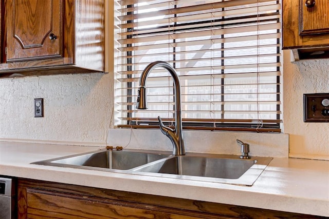 kitchen with a textured wall, light countertops, a sink, and brown cabinets