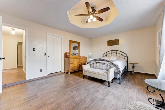 bedroom featuring light wood finished floors, a tray ceiling, and a textured ceiling