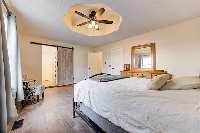 bedroom with a textured ceiling, a barn door, wood finished floors, visible vents, and a raised ceiling