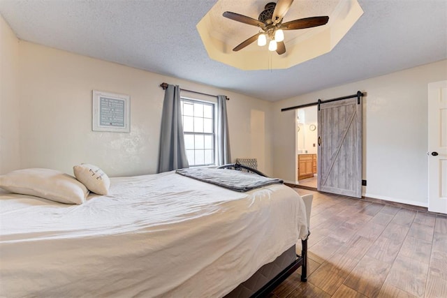 bedroom featuring a barn door, baseboards, wood finished floors, a tray ceiling, and a textured ceiling