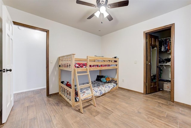 bedroom with a spacious closet, light wood finished floors, a ceiling fan, and baseboards