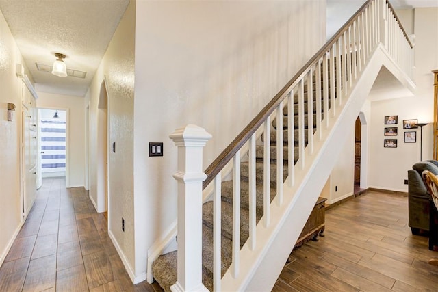 staircase featuring arched walkways, a textured ceiling, wood finished floors, and baseboards