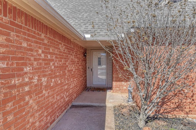 doorway to property with brick siding and roof with shingles