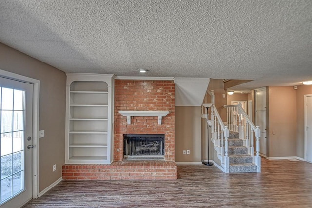 unfurnished living room featuring baseboards, stairway, wood finished floors, a brick fireplace, and built in shelves