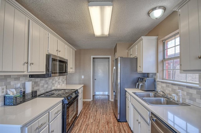 kitchen with appliances with stainless steel finishes, light countertops, a sink, and white cabinetry