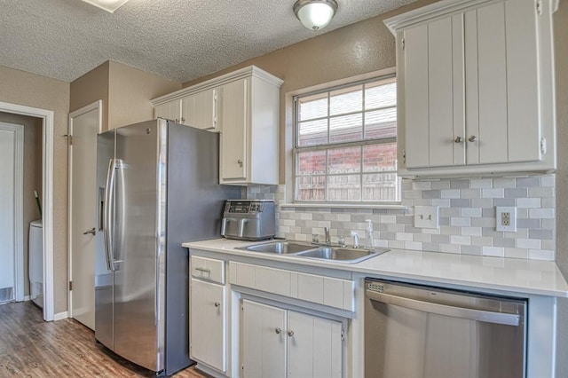 kitchen with stainless steel appliances, a sink, white cabinetry, light countertops, and decorative backsplash