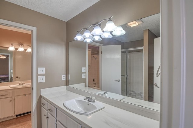 full bathroom with a textured ceiling, an enclosed shower, two vanities, and a sink