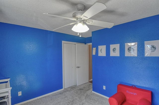 unfurnished room featuring a textured ceiling, a textured wall, carpet floors, a ceiling fan, and baseboards