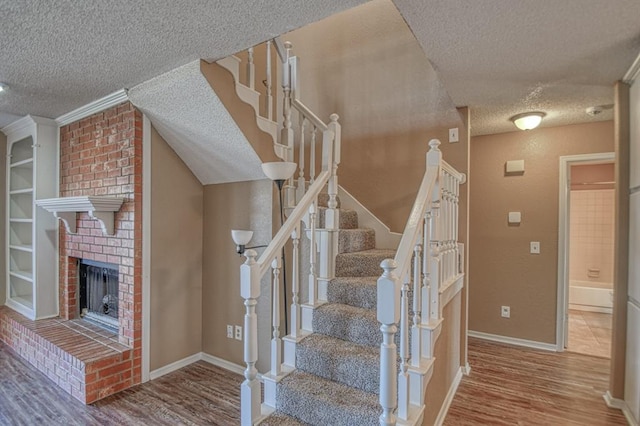 stairway featuring a fireplace, a textured ceiling, baseboards, and wood finished floors