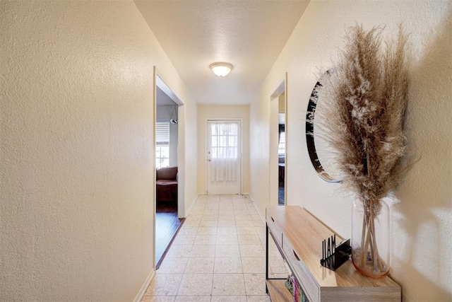 entryway featuring baseboards, light tile patterned flooring, and a textured wall