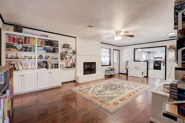 living area with a textured ceiling, dark wood-type flooring, a fireplace, visible vents, and a ceiling fan