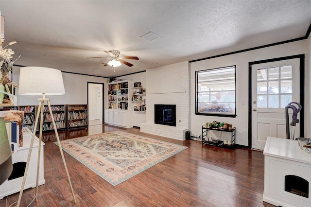 living room with ceiling fan, a fireplace, a textured ceiling, and wood finished floors