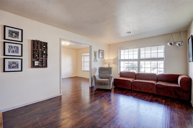 living area with visible vents, a textured ceiling, baseboards, and wood finished floors