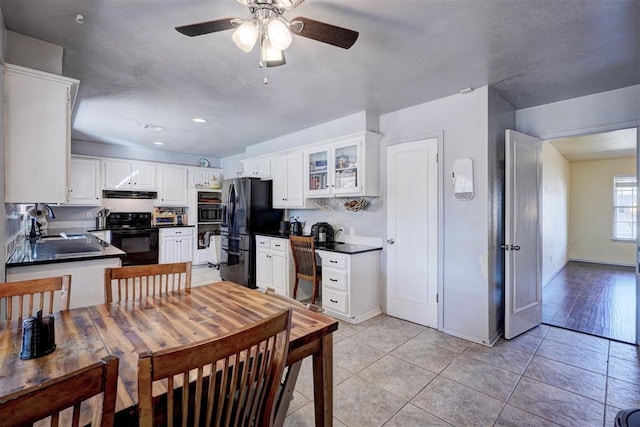 kitchen with dark countertops, black appliances, glass insert cabinets, and exhaust hood