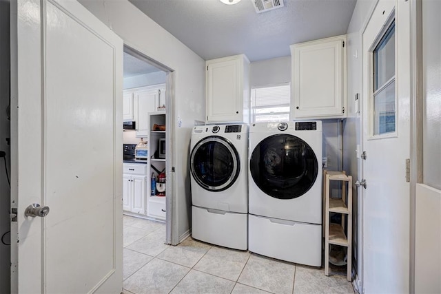 clothes washing area with visible vents, cabinet space, washer and clothes dryer, and light tile patterned floors