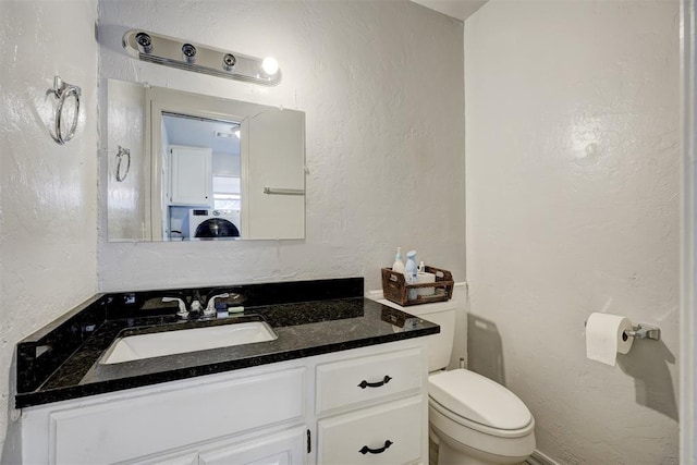 bathroom with a textured wall, washer / dryer, vanity, and toilet