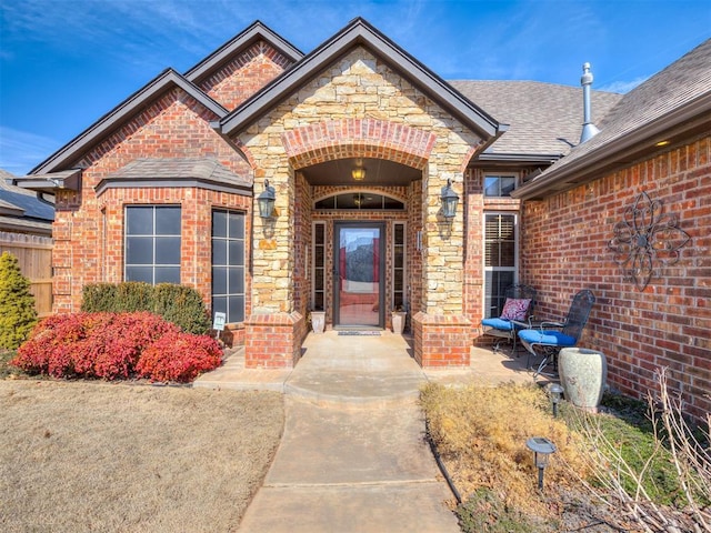 property entrance with stone siding, roof with shingles, and brick siding