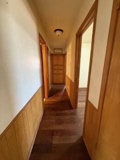 hall featuring a wainscoted wall, dark wood-type flooring, and wood walls