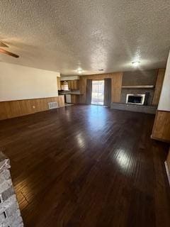 unfurnished living room with wooden walls, dark wood finished floors, wainscoting, a textured ceiling, and a fireplace