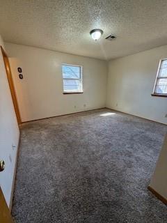 empty room with a healthy amount of sunlight, visible vents, dark carpet, and a textured ceiling