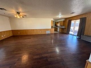 unfurnished living room with a textured ceiling, ceiling fan, a wainscoted wall, dark wood-type flooring, and wood walls