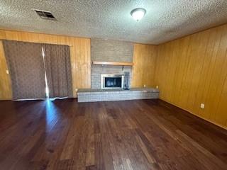 unfurnished living room featuring a textured ceiling, a fireplace, dark wood finished floors, and visible vents