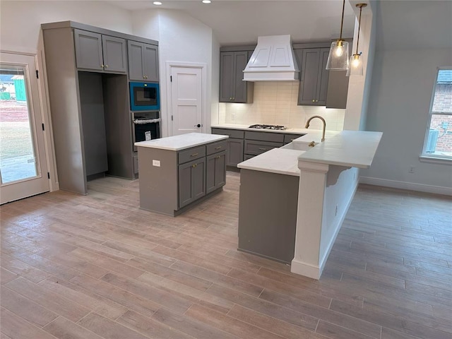 kitchen with a peninsula, gray cabinets, stainless steel appliances, premium range hood, and a sink