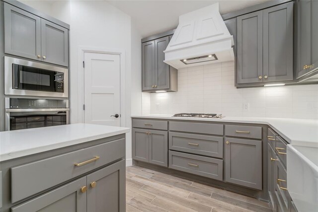 kitchen with premium range hood, oven, gray cabinetry, and built in microwave