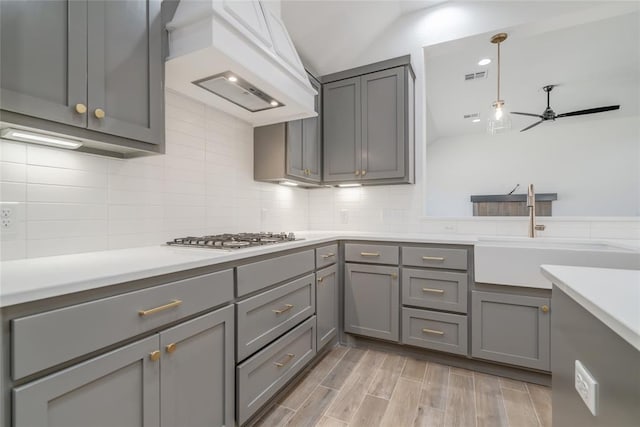 kitchen with gray cabinetry, custom exhaust hood, visible vents, and a sink