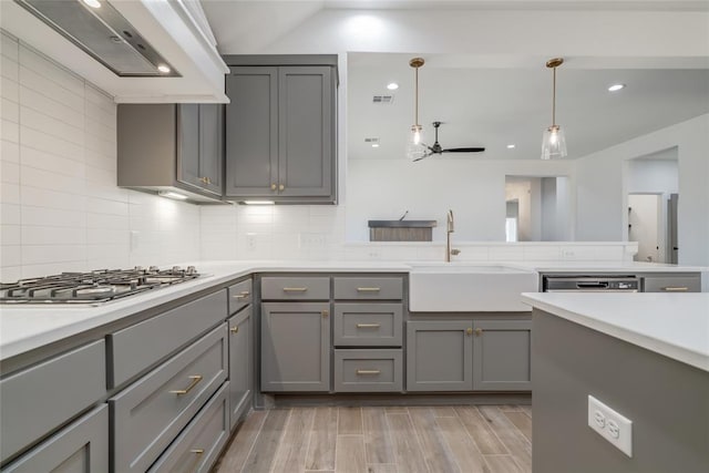 kitchen featuring a sink, wall chimney range hood, ceiling fan, light countertops, and gray cabinets
