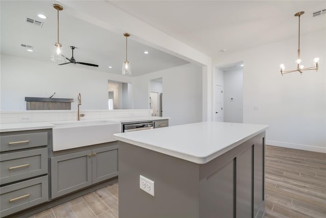 kitchen with gray cabinetry, ceiling fan with notable chandelier, a sink, and wood finish floors