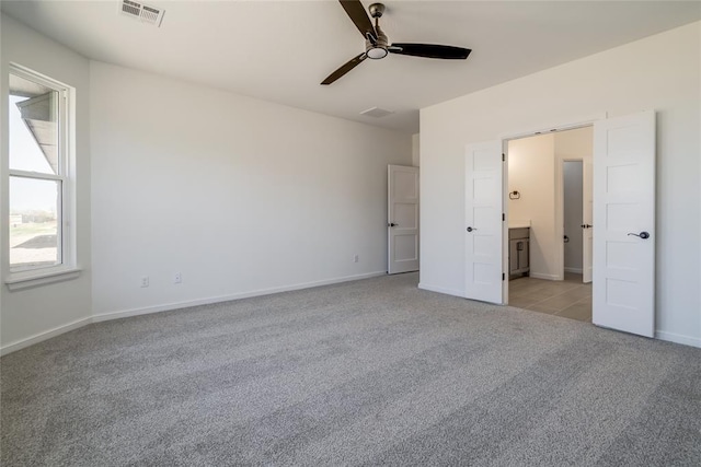 unfurnished bedroom featuring baseboards, light carpet, ensuite bath, visible vents, and ceiling fan
