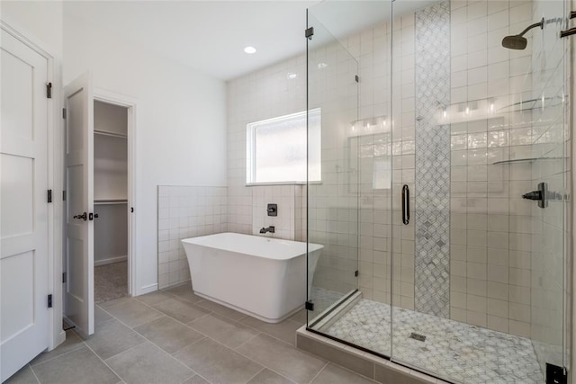 bathroom with tile patterned flooring, a spacious closet, a freestanding bath, tile walls, and a stall shower