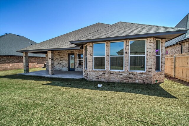 back of property with a lawn, a patio, roof with shingles, fence, and brick siding