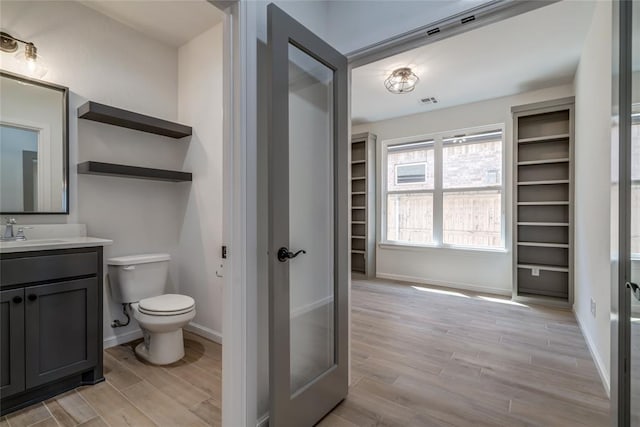 bathroom with toilet, vanity, wood finished floors, and baseboards