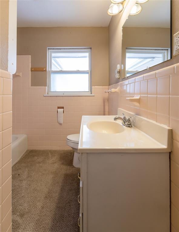 bathroom with a wainscoted wall, tile walls, toilet, vanity, and a bath