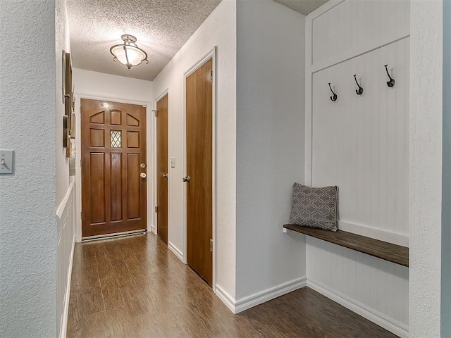 doorway featuring a textured ceiling, a textured wall, wood finished floors, and baseboards