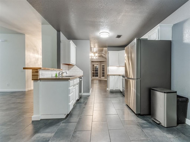 kitchen with stainless steel appliances, visible vents, decorative backsplash, white cabinetry, and a sink