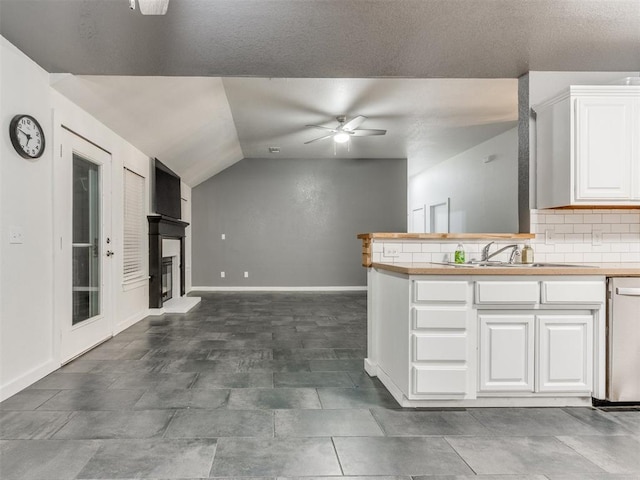 kitchen with light countertops, a fireplace with raised hearth, decorative backsplash, white cabinets, and dishwasher