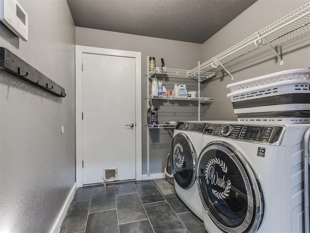 clothes washing area with a textured ceiling, laundry area, dark tile patterned flooring, baseboards, and washer and dryer