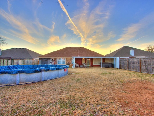 rear view of property featuring a yard, a fenced backyard, and a fenced in pool