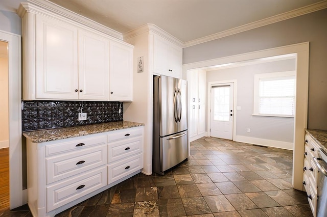 kitchen featuring white cabinets, backsplash, freestanding refrigerator, dark stone counters, and crown molding