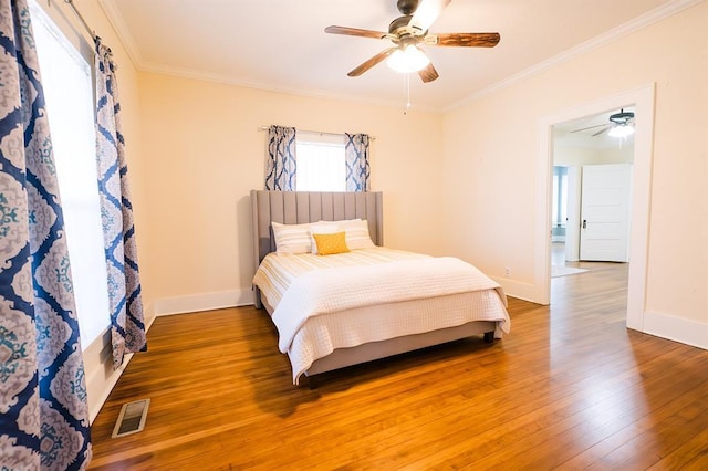 bedroom with baseboards, wood finished floors, visible vents, and crown molding