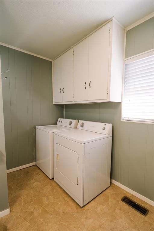 clothes washing area featuring washer and clothes dryer, cabinet space, visible vents, and baseboards