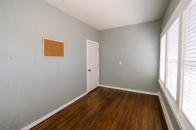 spare room featuring a wealth of natural light, baseboards, and dark wood-style flooring