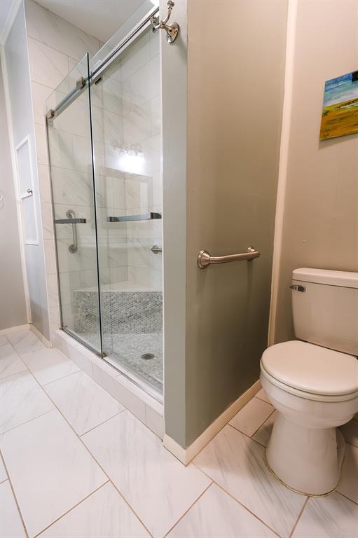 bathroom featuring a stall shower, marble finish floor, baseboards, and toilet