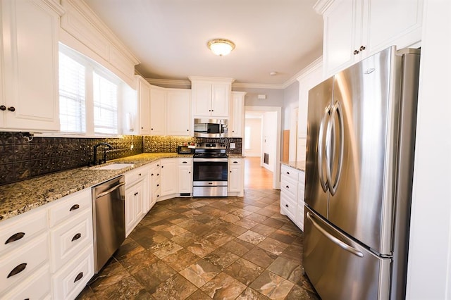 kitchen with light stone counters, appliances with stainless steel finishes, a sink, and white cabinetry