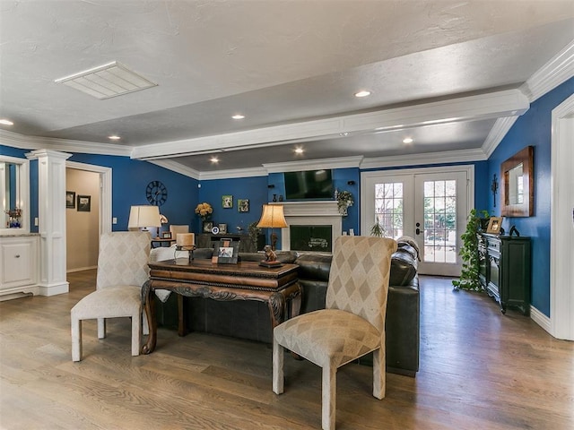 living area featuring wood finished floors, decorative columns, a fireplace, crown molding, and beamed ceiling